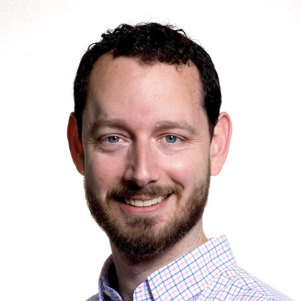 Ryan Merkley's headshot. A person with short hair and a beard, wearing a collared shirt, smiles at the camera.