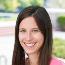 Betsy Cooper's headshot. A person with long, dark hair is outside smiling at the camera.