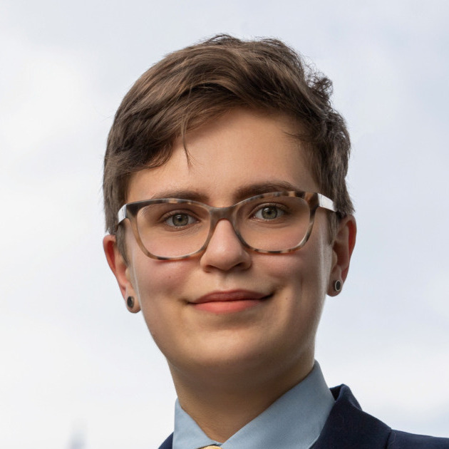 Eleanor Tursman's headshot. A person with short hair, wearing glasses and earrings, smiles at the camera.