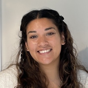 Kateri Gajadhar-Smith's headshot. A person with long, dark, curly hair smiles at the camera.