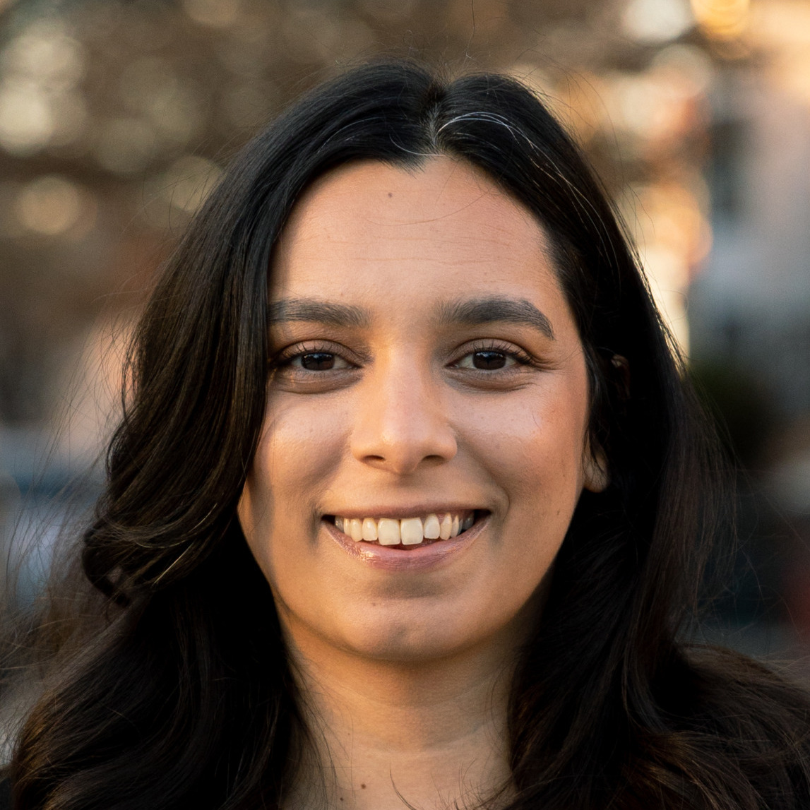 Shanthi Bolla's headshot. A person with long, dark hair and side bangs is outside, smiling at the camera.