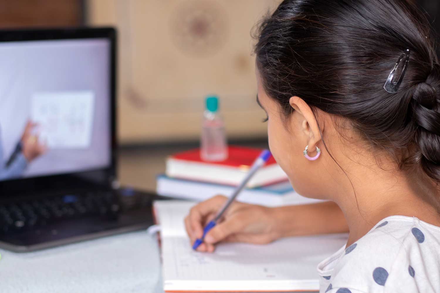A photograph of a girl looking at a laptop and writing notes on paper.