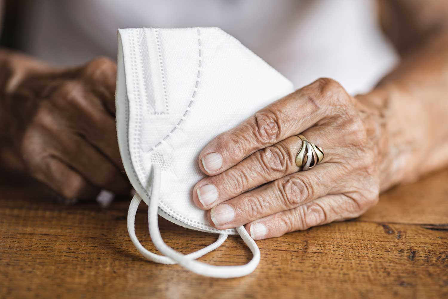 A photograph of an older person's hands resting on a COVID-19 mask