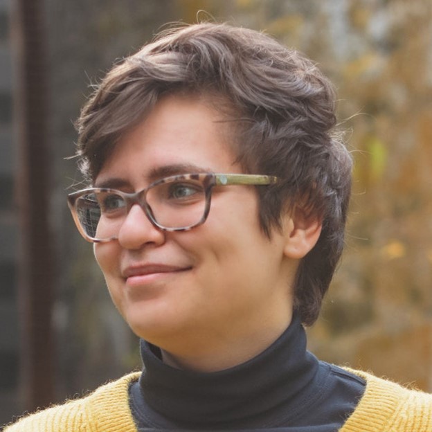 Eleanor Tursman's headshot. A person with short hair, wearing glasses and a turtleneck, smiles at the camera.