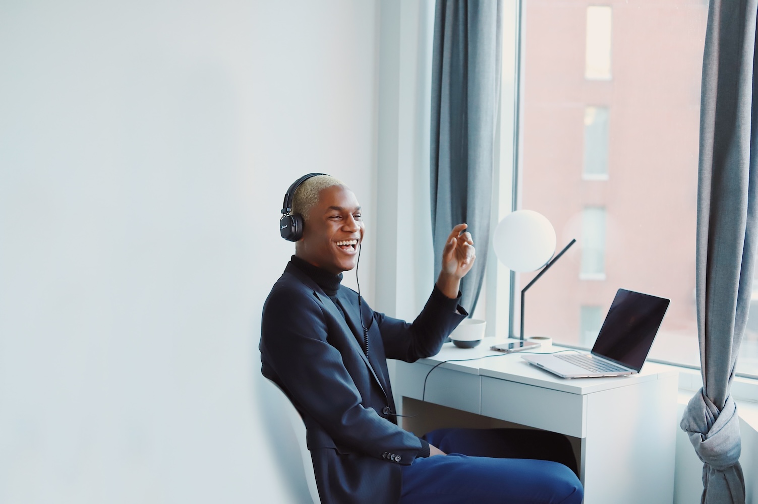 A photo of a person sitting at a desk by a window smiling while on a call.