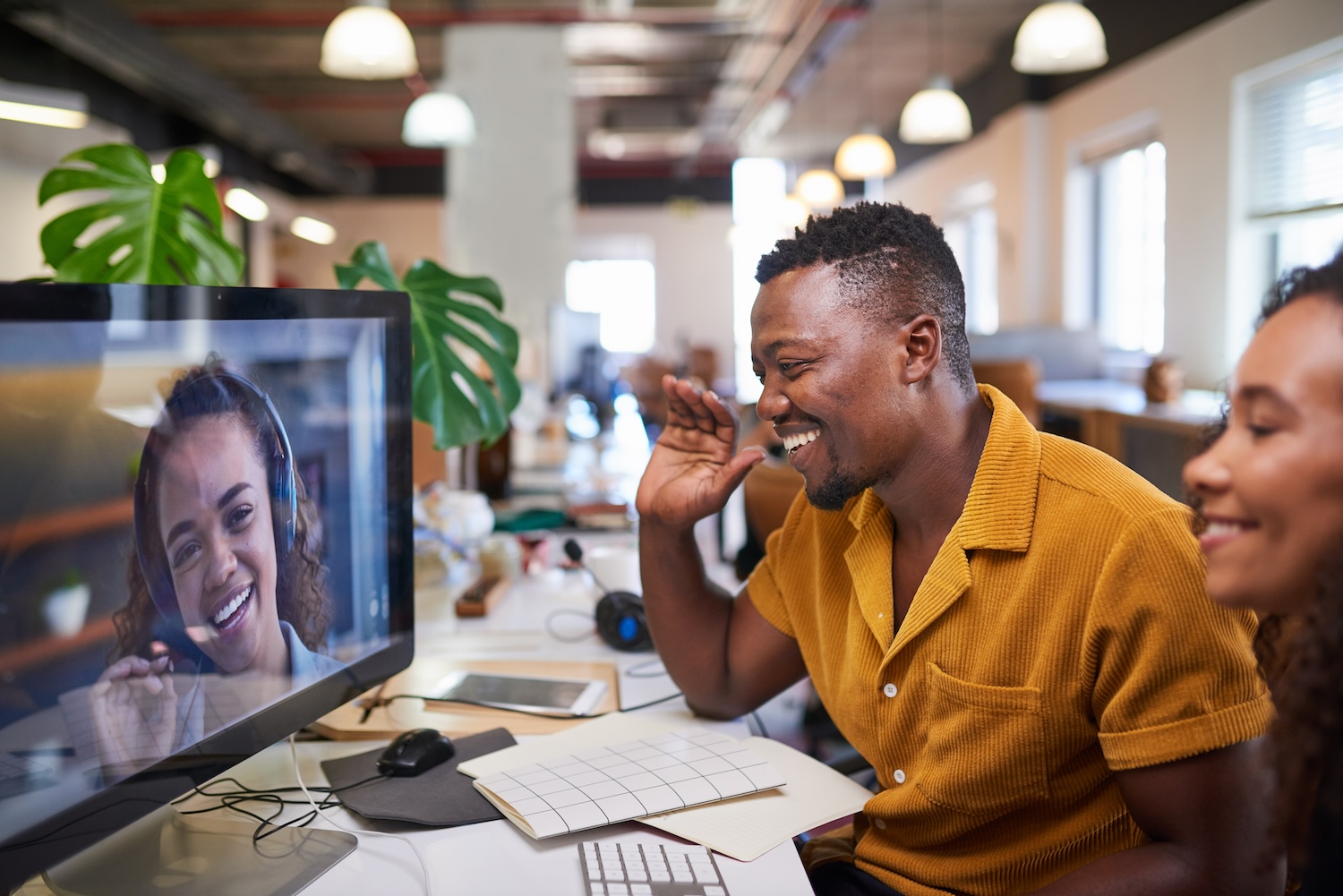 Two South Africans sit in an office video conferencing with their colleague on a desktop computer.