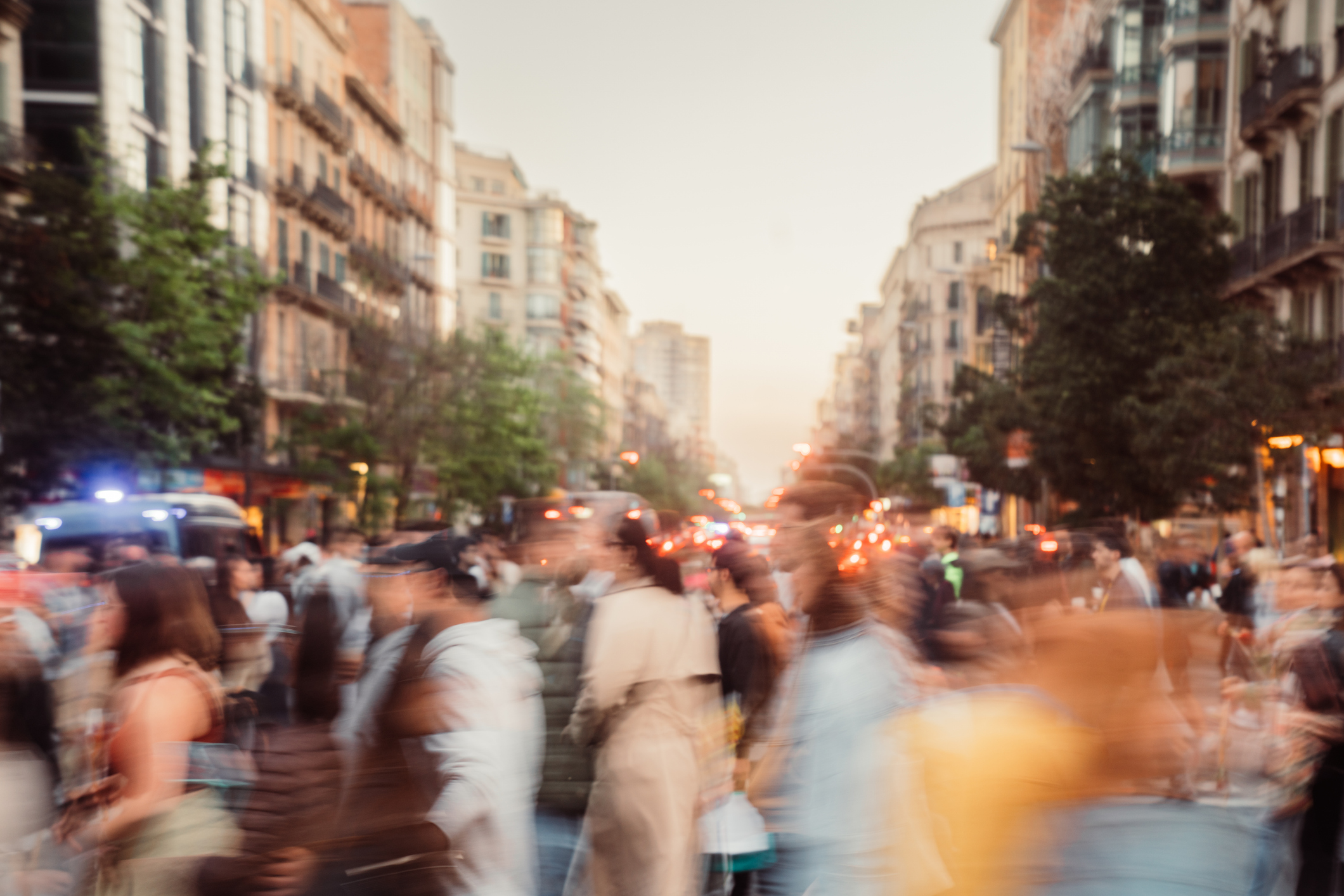 A photograph of a blurred crowd of people and cars on a busy city sidewalk.