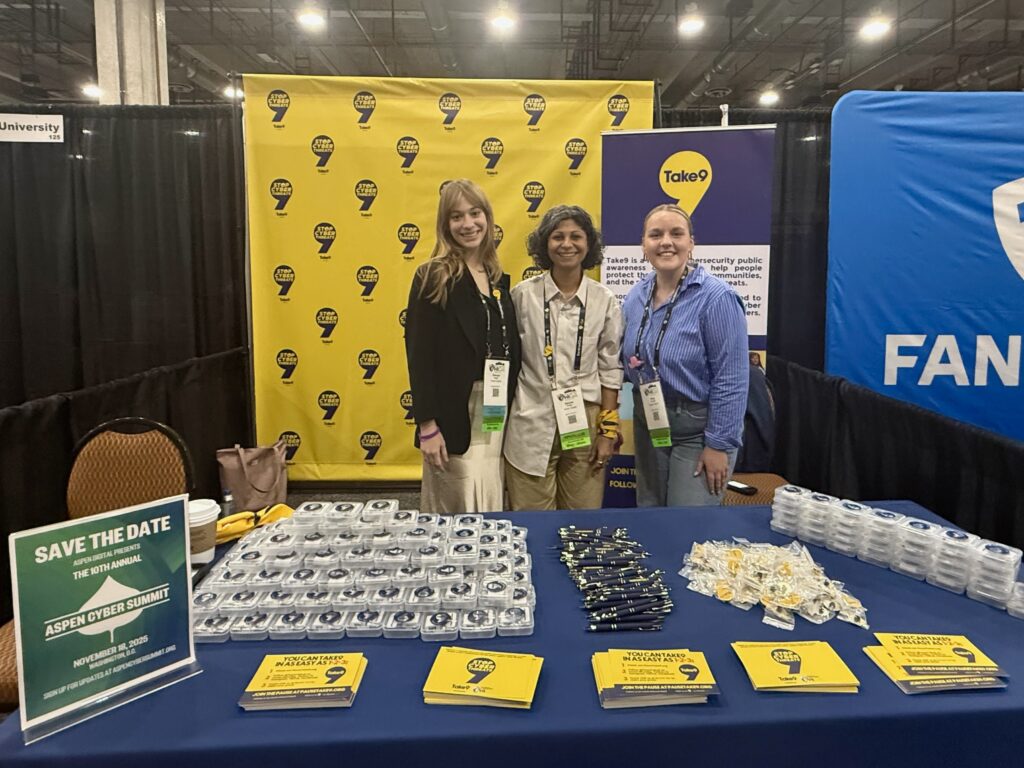 A photo of Aspen Digital staff behind the Take9 career fair booth at WiCyS.
